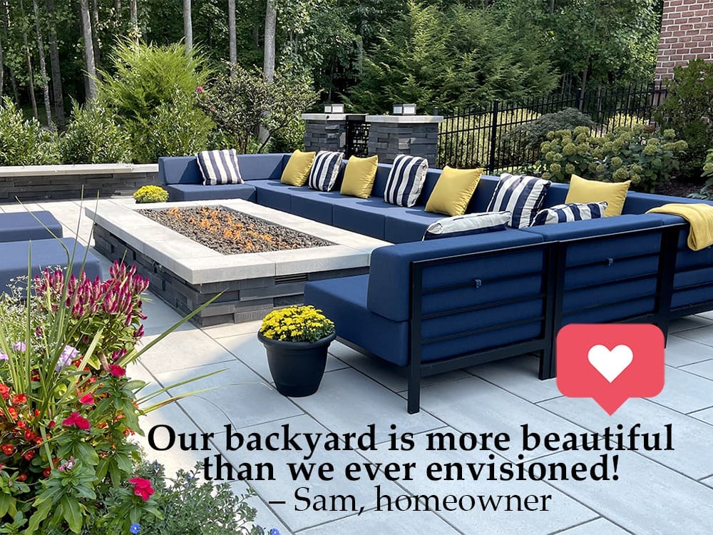 A luxurious backyard patio featuring a large fire pit surrounded by L-shaped navy blue seating with yellow and white throw pillows. The space is adorned with various plants, and a quote from the homeowner, Sam, praises the beauty of the backyard.