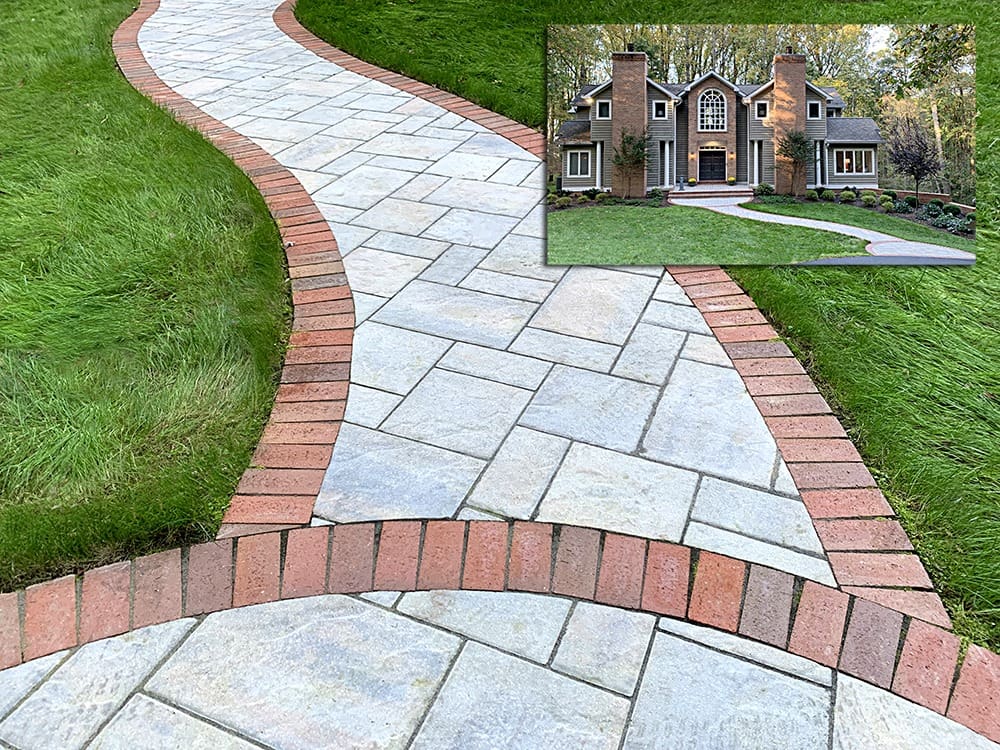 A winding stone pathway edged with red bricks curves through a lush, green lawn. In the upper right corner, there is a small inset image of a large house with tall, brick chimneys and a well-manicured front yard.